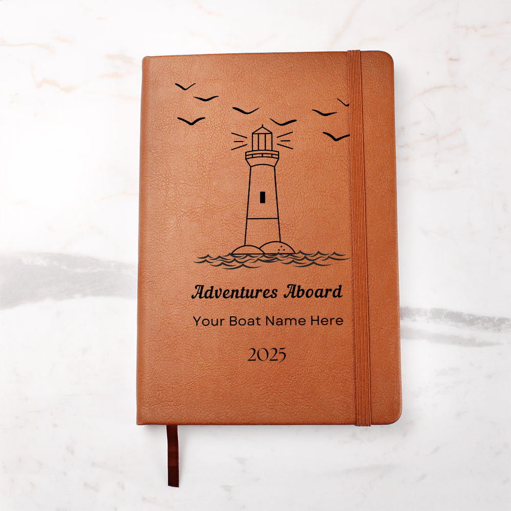 6 inch by 9 inch book with a light brown leather cover. On the cover is a. line drawing of a lighthouse with line drawings of birds in the sky. The words on the front say "Adventures Abroad" Under these words is a space for buyer to insert their boat name. Under that is the year 2025. You can see a ribbon bookmark and also a brown elastic that holds the journal shut.